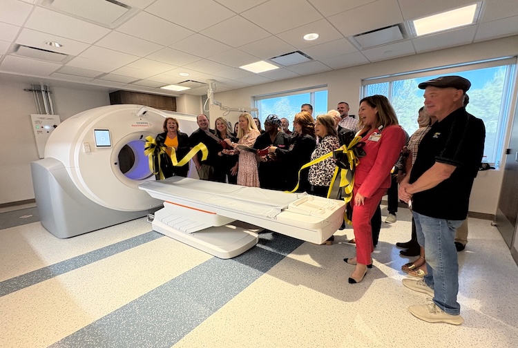 A diverse group of hospital employees and community members smile during a ribbon cutting event.