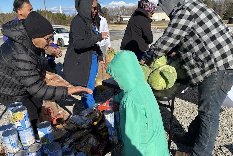 People bundled up in winter coats, standing near a table and getting fresh produce and canned goods.