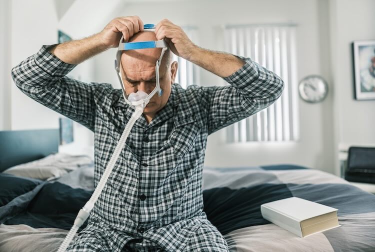 Older man getting ready to sleep during the day with a CPAP machine in bed.