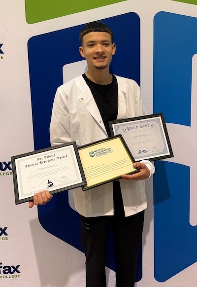 Caleb stands in a medical white coat with his degrees.