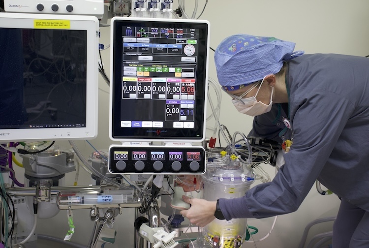 Person in scrubs and a facemask works on equipment before a surgery