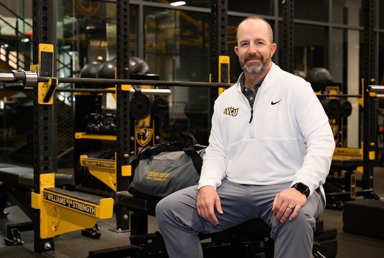Dr. Cheatham sits on a weight lifting bench in the student athlete gym