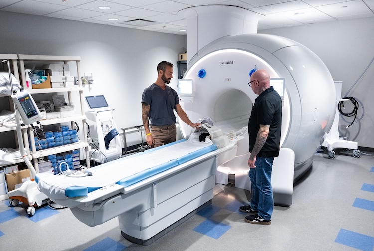 Two men stand near an MRI machine