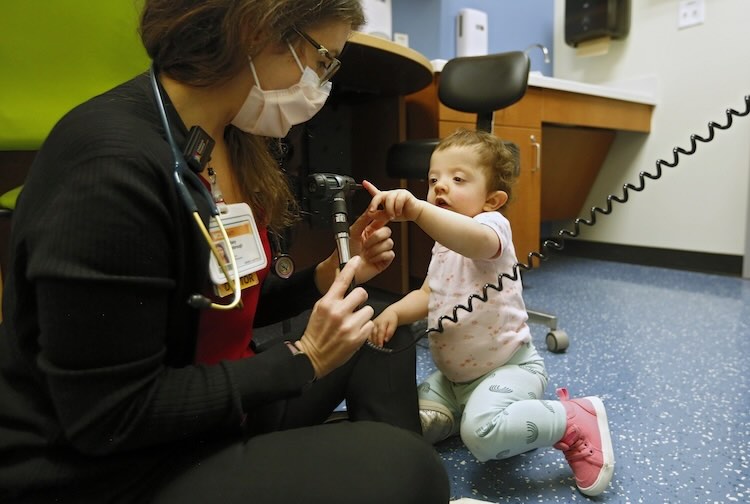 Dr. Kimbrough sits on the floor and lets a toddler play with her equipment