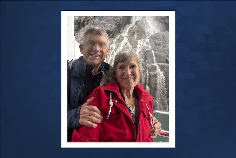 Chal and Catherine smile in rain coats in front of a waterfall.