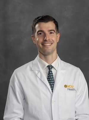 Dr. Layon wears a green tie with a white button up shirt under his white medical coat.