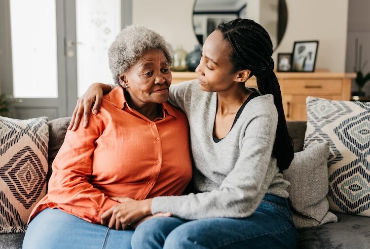 Young woman hugging and comforting mother on sofa at home
