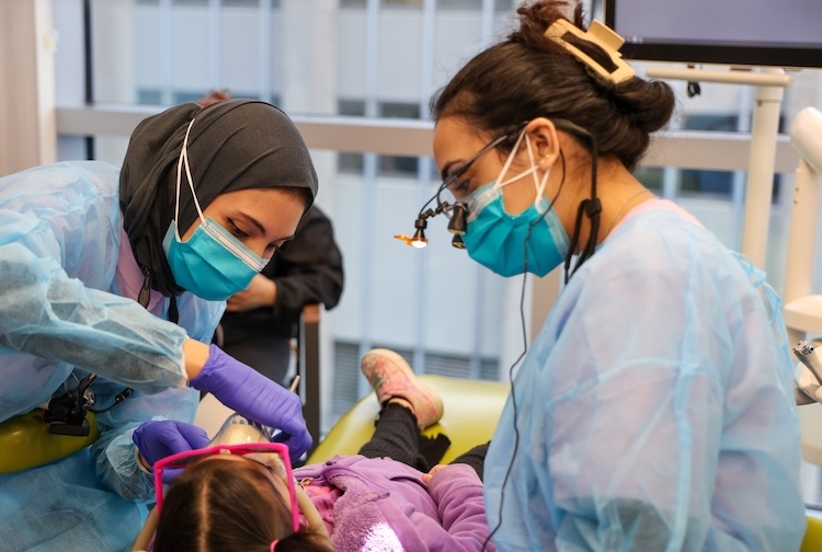 Two female dental students check a little girl’s teeth