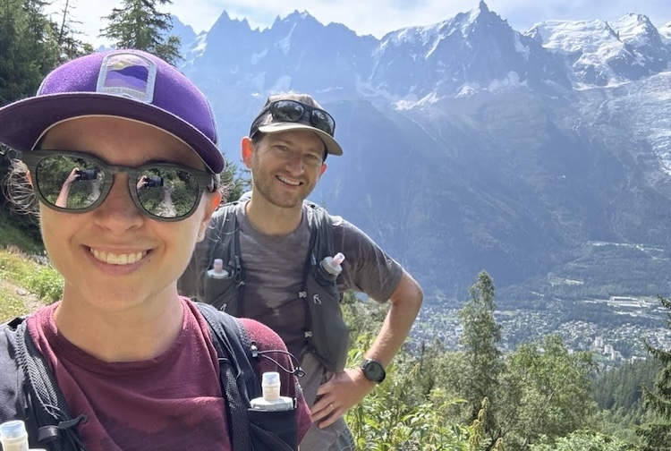 Desiree standing with her husband Brad on a hiking trail with a large mountain behind them.
