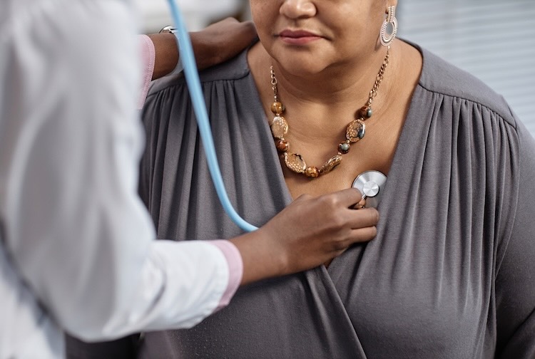 Cropped photo of unrecognizable female patient at check up in clinic with doctor pressing stethoscope to her chest