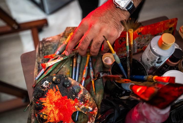 Dr. Khan's grabs a brush on a table with a bunch of paints and palettes