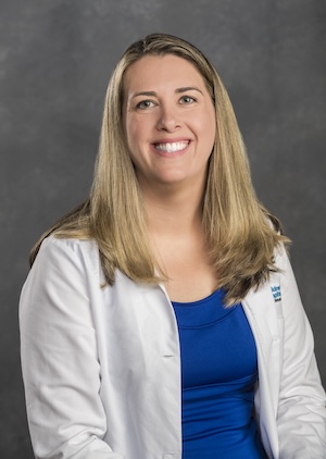 Dr. Strauss is wearing a medical white coat and blue shirt.