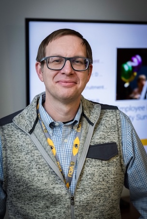 Dr. Downs in a grey sweater vest in front of a projector screen.