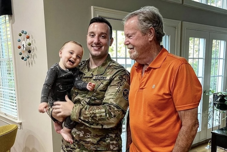 Evan is dressed in his army uniform while standing with his son and father