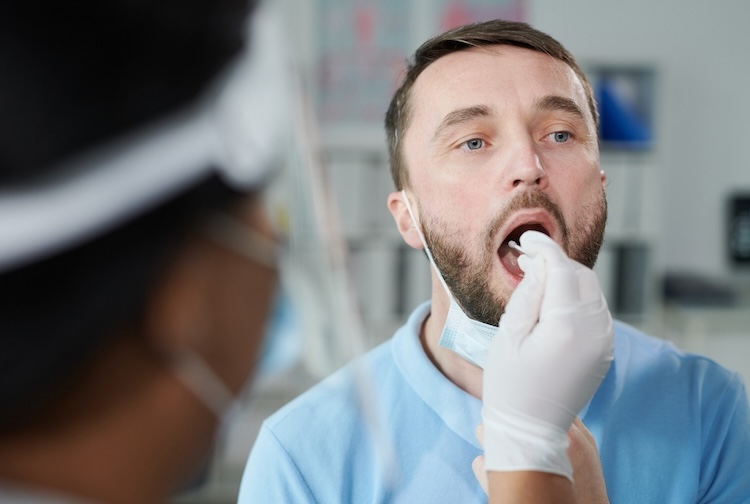 young male patient being tested for covid with oral swab held by gloved female nurse