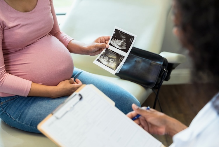 Doctor going through ultrasound with pregnant patient, who is holding picture of ultrasound of fetus in utero.