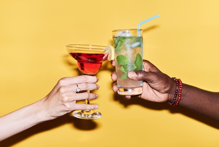 Two arms clinking drinks together with cocktails