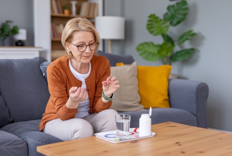 An older woman is sitting on a sofa, preparing to take her medication