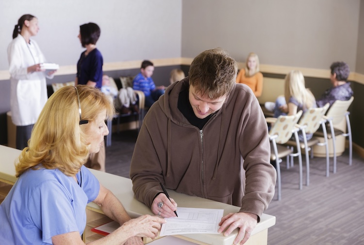 Man fills out medical paperwork with receptionist in a busy waiting room