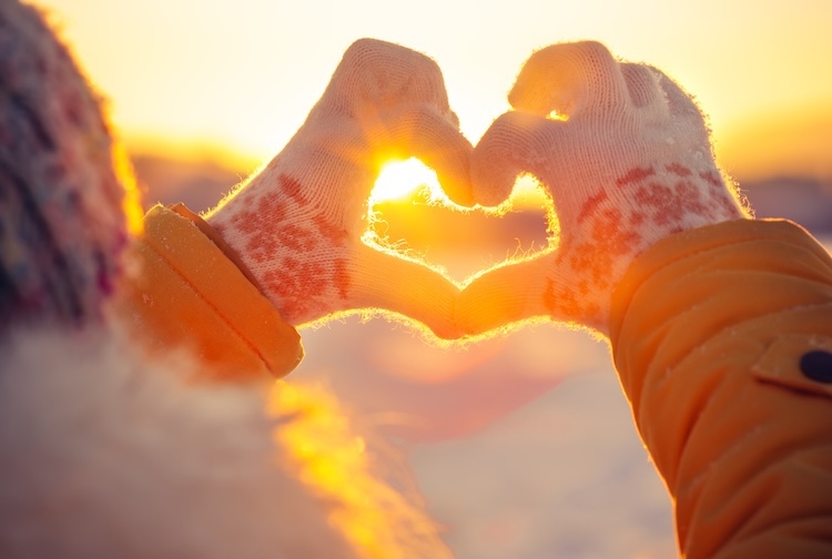 Woman wearing winter gloves on makes a heart symbol shape with her hands