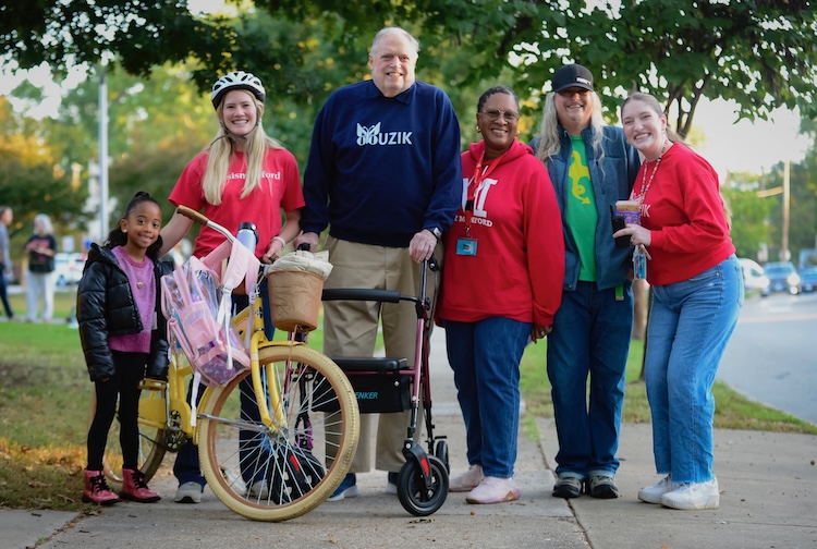 Greg stands with several students and staff next to a bike