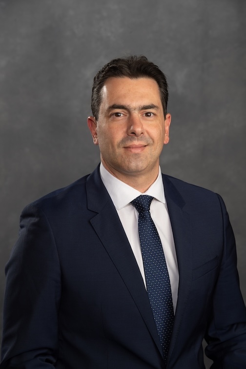 Dr. Mazzini is wearing a black suit and white shirt with a navy blue tie.