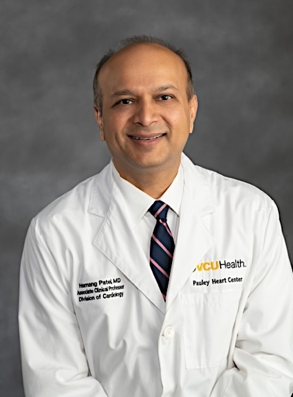 Dr. Patel wears a medical white coat and navy tie with pink stripes