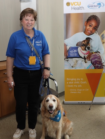 Dogs on Call volunteer and therapy dog stands near sign for the program