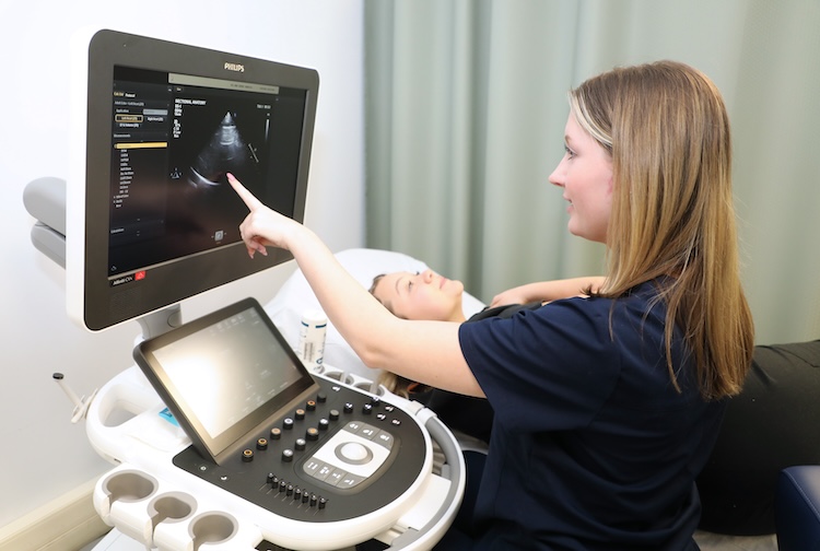 A professor and students look at the images of a student’s heart on a sonography machine.