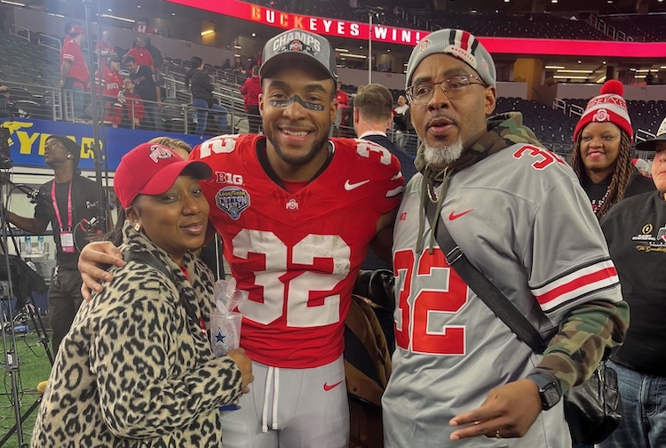 Trent wears a matching football jersey with his son TreVeyon while standing with his wife in a leopard print jacket.