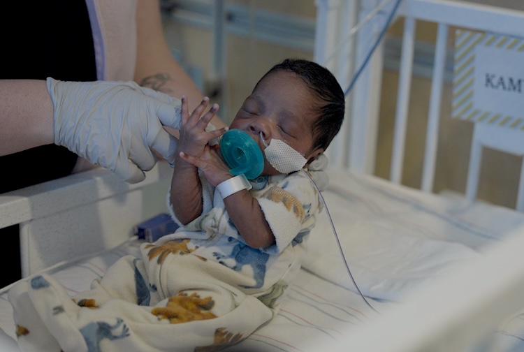 Baby Kamryn held up by a nurse in his NICU crib