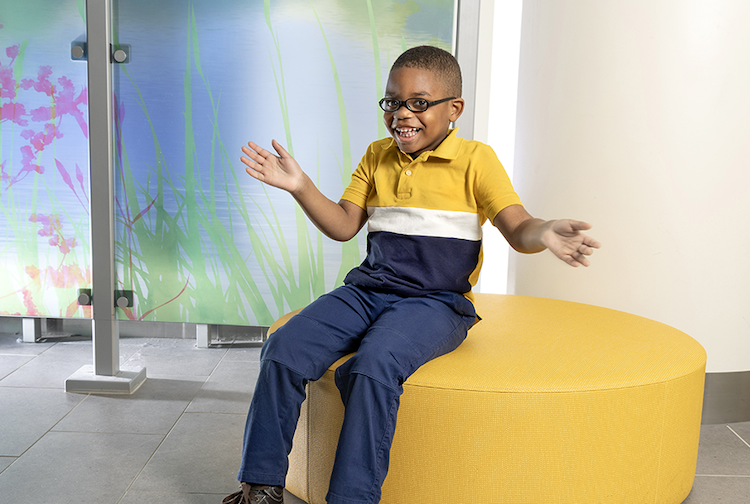 Khaza sitting on a yellow round ottoman.