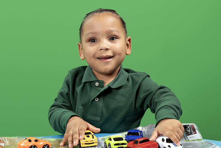 Toddler wears a green polo shirt while playing with toy trucks