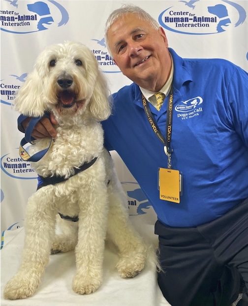 Dr. Levy is wearing a blue shirt and is standing next to a white labordoodle.