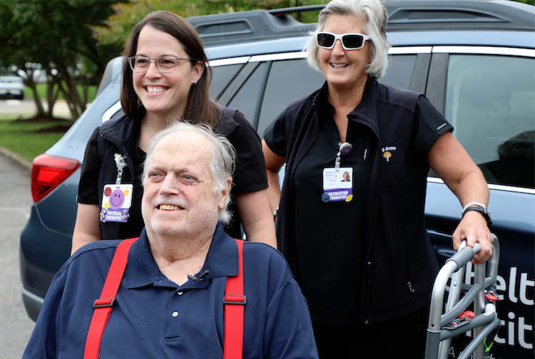 Muzik sits in a wheelchair near his Sheltering Arms Institute care team