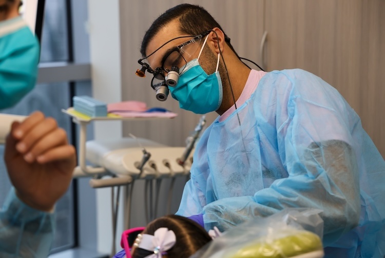 Male dental student checks on the teeth for a small girl who has bows in her hair