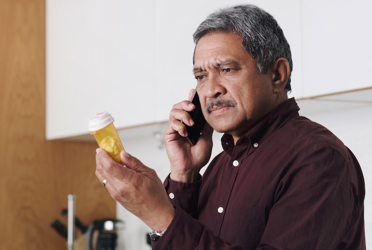 senior man reading the label on a medicine container and talking on a cellphone
