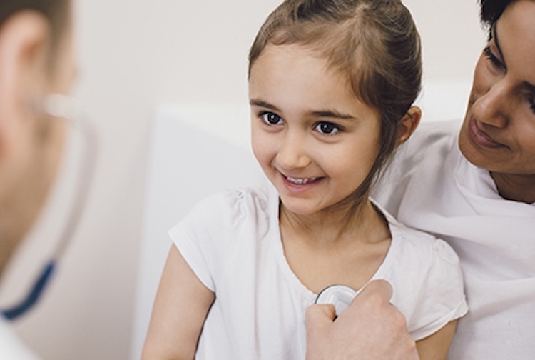 Doctor holding stethoscope to child's chest while she sits in her mother's lap