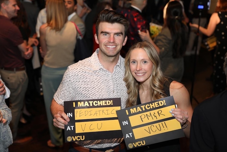 Man and woman hold signs with VCU on them
