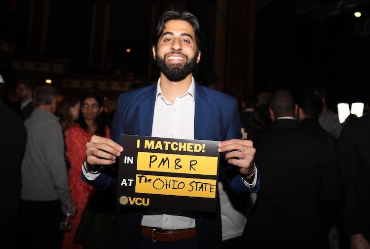 Man in a suit holding up a sign and smiling