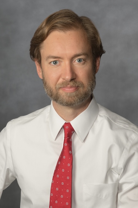 Dr. Barrett wearing a white button up shirt with a red tie.
