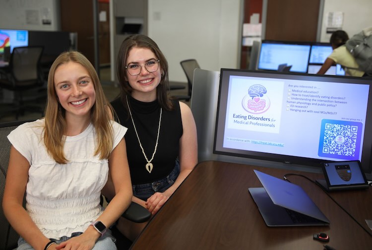 Two medical students sitting next to a computer montior with a presentation on the screen.