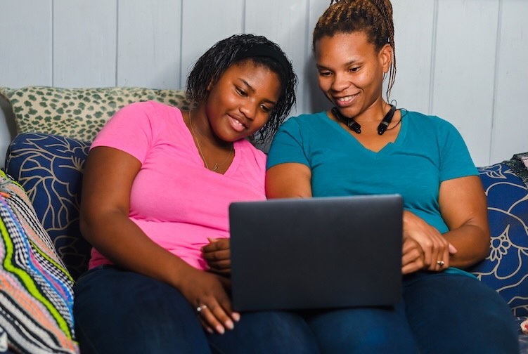 Black mother and teen daughter hang out together in the living room using a laptop computer together