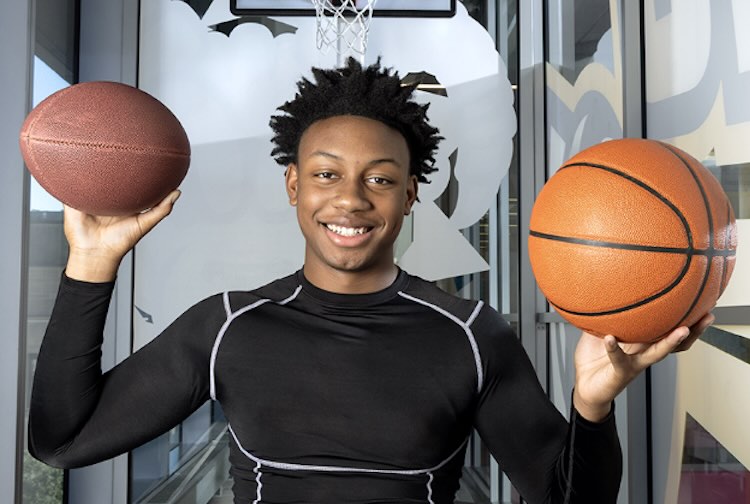 Teenage holding a football in one hand and basketball in the other.