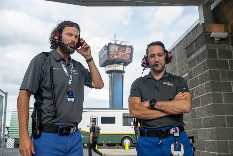 Two doctors with headphones protecting their ears stand outside of a medical center at the Richmond Raceway.