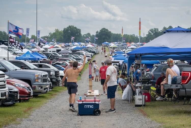 Richmond Raceway parking lot filled with trucks, flags and people playing cornhole.