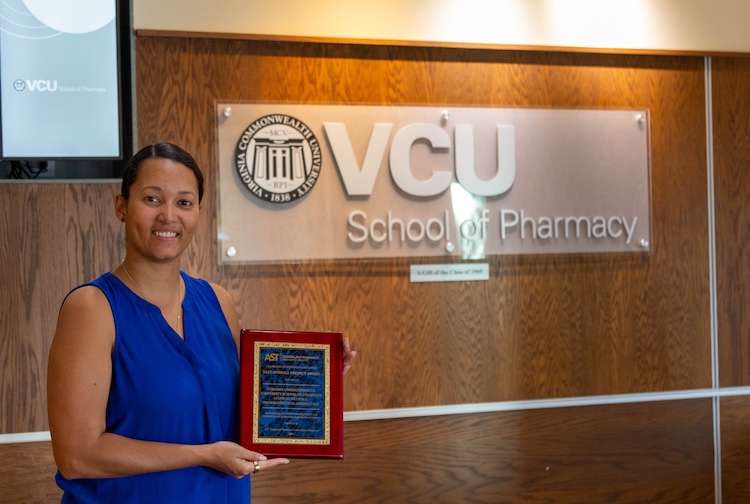 VCU pharmacy student Nina Chatman stands in front of school sign with her award.