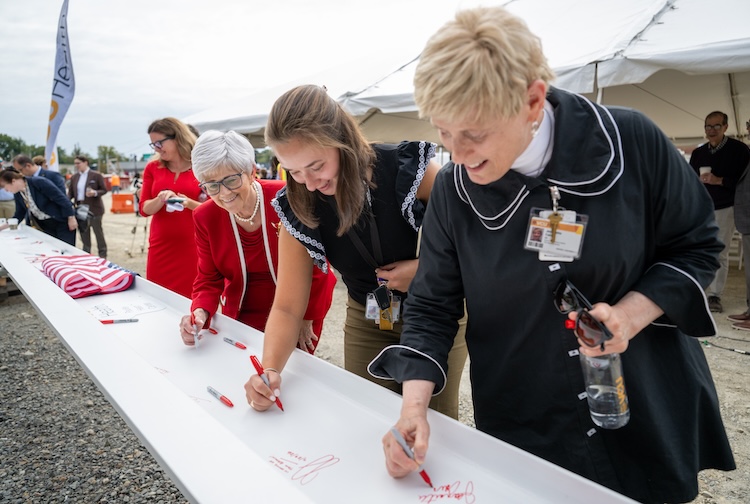 Group of women sign a beam before it is placed at the top of a new building for VCU Health