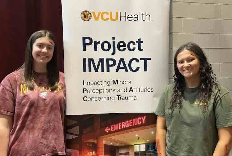 Two high school seniors pose next to a VCU Health sign for Project IMPACT.