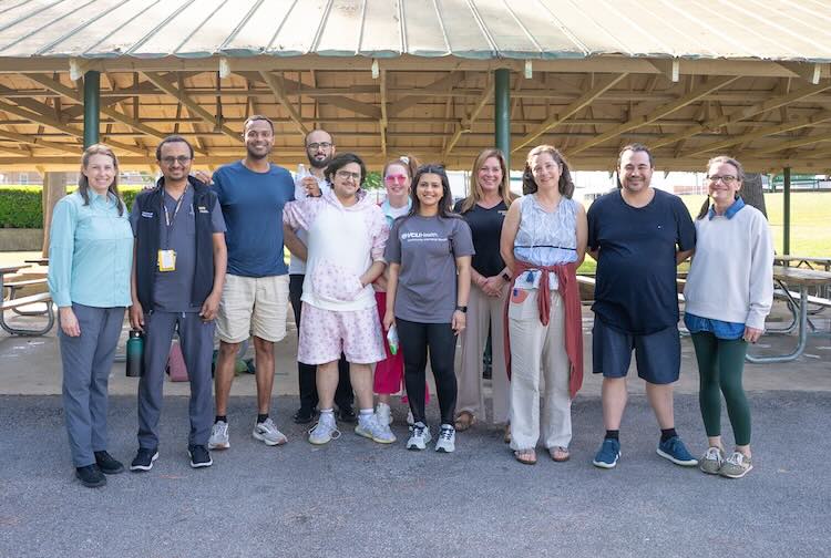 A group of medical residents, faculty and staff from VCU Health Community Memorial Hospital stand together smiling for a photo beneath a park pavilion.